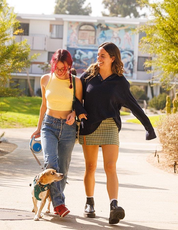 Two students walk with arm linked while walking a dog in Scott courtyard